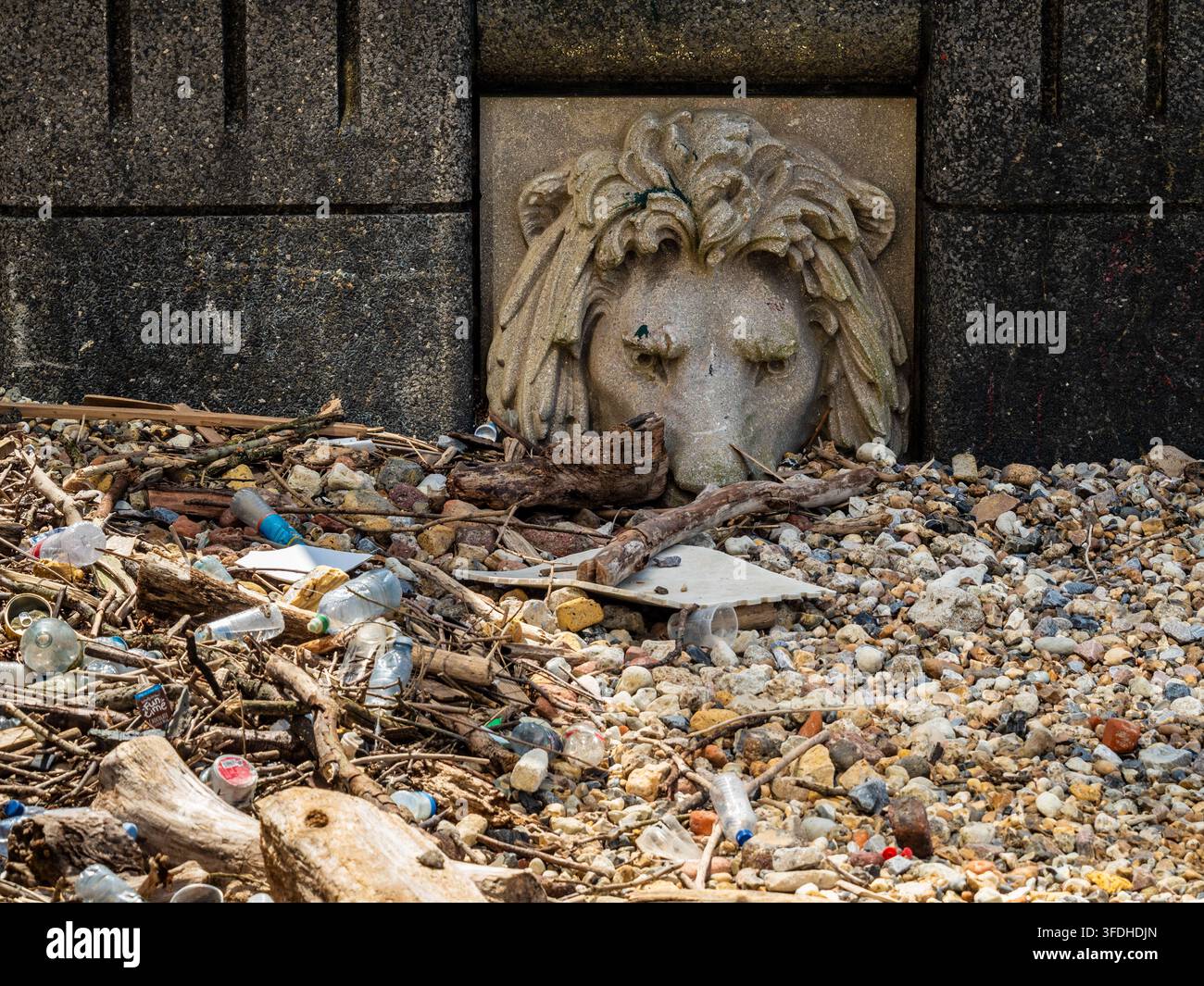 Tête de lion décorative en pierre érodée encastrée dans le mur de la berge de la Tamise au centre de Londres, partiellement enterrée sous des galets. Londres. Royaume-Uni Banque D'Images
