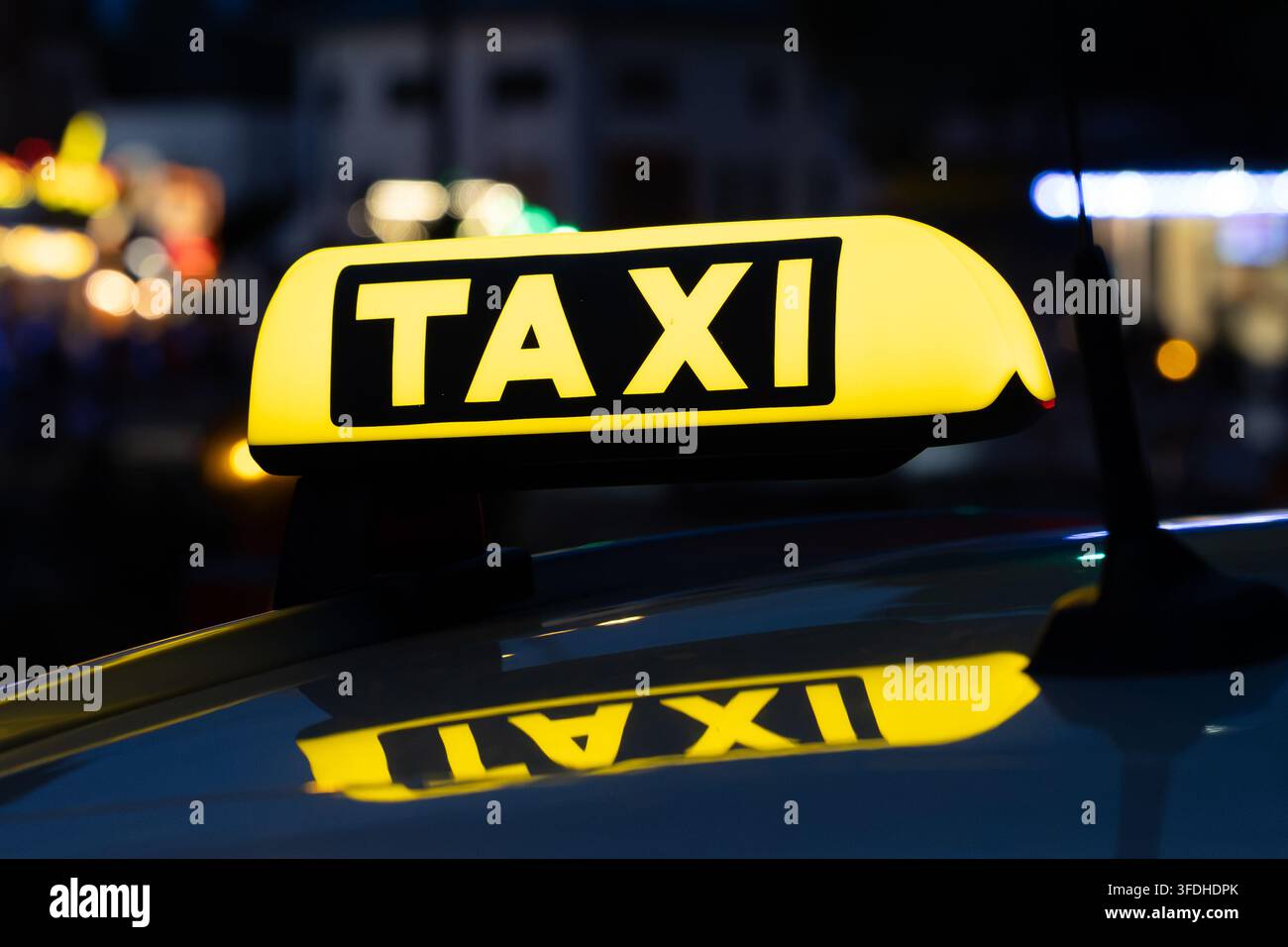 Taxi attendant devant une fête foraine allemande la nuit, avec des lumières colorées de la fête foraine et des attractions en arrière-plan. Banque D'Images
