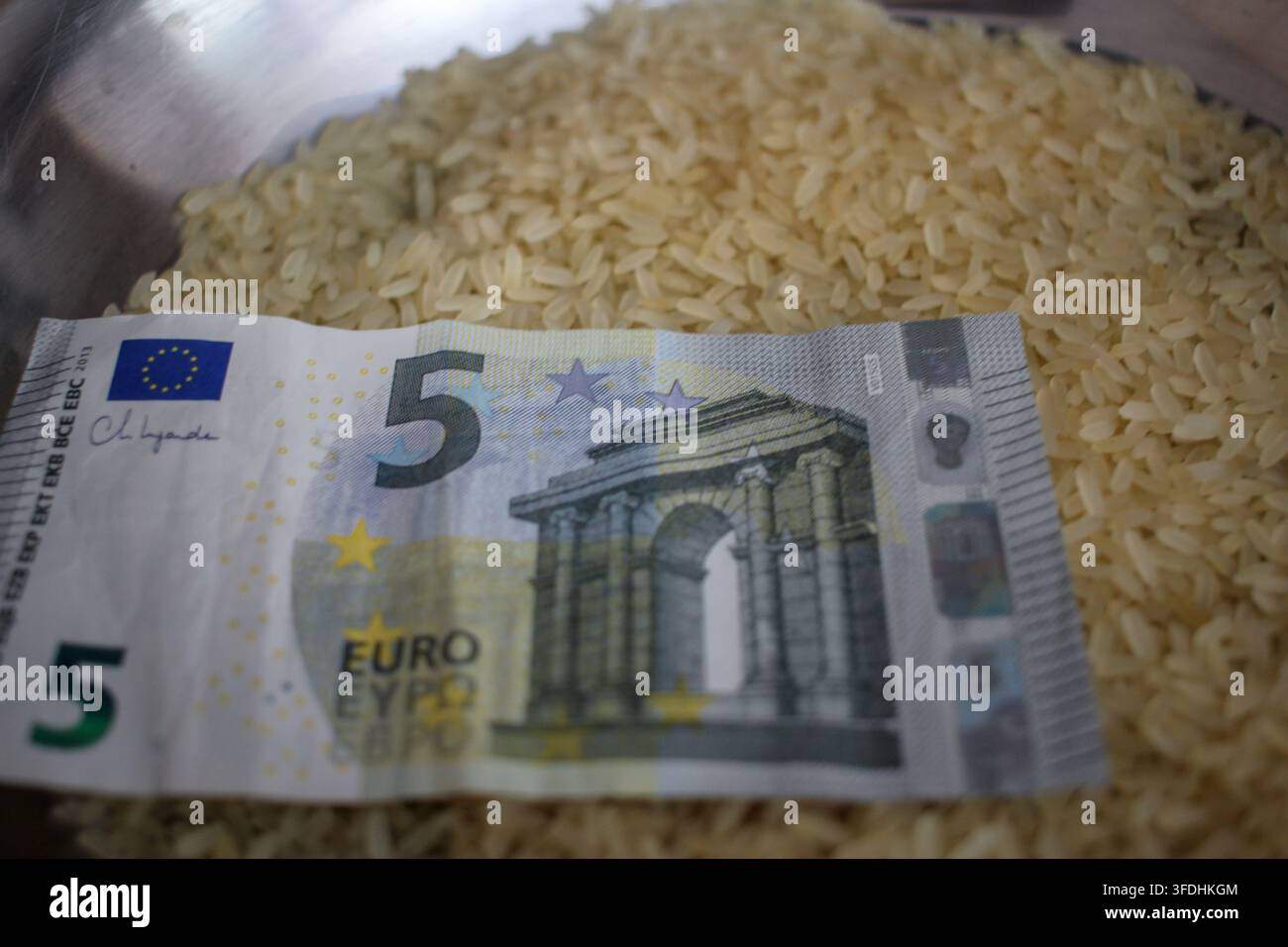 Un gros plan d'un billet de cinq euros posé sur des grains de riz blanc cru, représentant l'inflation alimentaire, la hausse des coûts agricoles, la crise alimentaire mondiale Banque D'Images