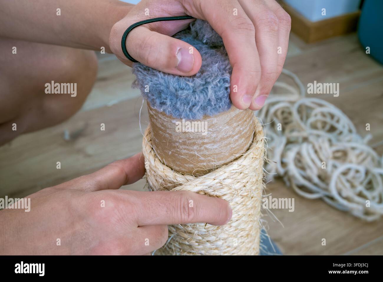 Les mains remplacent une corde en sisal usée sur un poteau à gratter, la fixant autour d'une surface en carton cylindrique effilochée avec un cordon lâche à proximité Banque D'Images