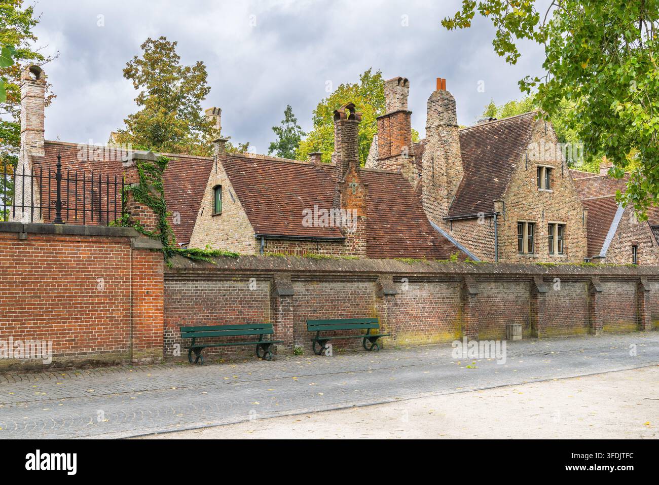 La ville de Bruges en Belgique, Europe. Bâtiments historiques européens en brique avec cheminées ornées et toits en terre cuite derrière un long mur de briques et des bancs Banque D'Images