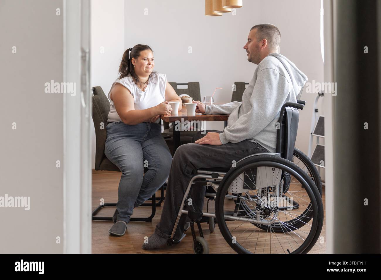 Homme en situation de handicap profitant d'une pause café et d'une conversation avec son assistant personnel dans un cadre domestique. Thème d'inclusion sociale. Banque D'Images