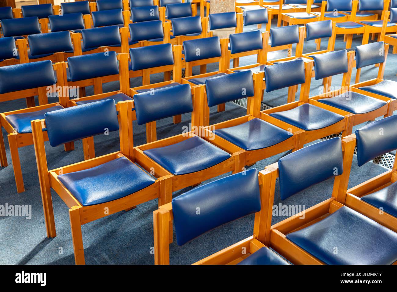 Une vue en angle intérieur de chaises en bois vides dotées d'assises et de dossiers en cuir bleu, disposées en rangées sur un tapis bleu. Banque D'Images