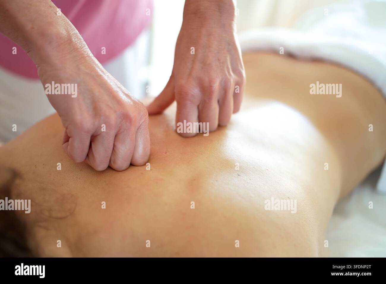 Thérapeute effectuant un massage des tissus profonds du dos sur un client adulte de sexe masculin dans une salle de traitement lumineuse avec lumière naturelle, pression ciblée sur les muscles, calme Banque D'Images
