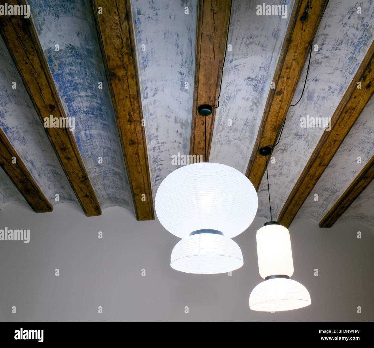 Des lanternes en papier contemporaines sont suspendues à un plafond présentant des poutres en bois apparentes avec une finition blanche et bleue texturée, mettant en valeur un mélange unique de vieux Banque D'Images