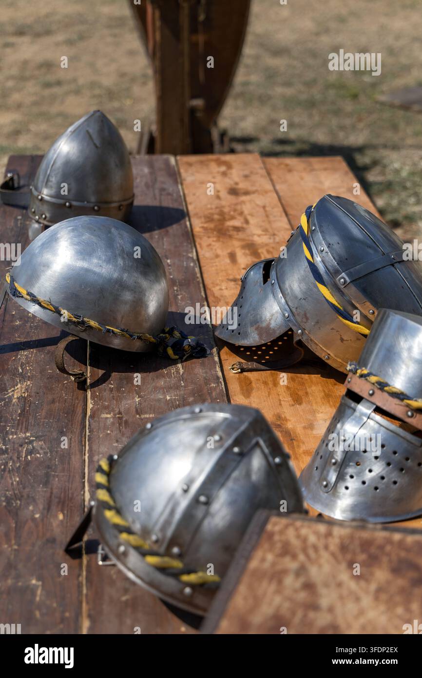 Casques d'acier de chevalier médiéval exposés sur une table en bois lors d'une reconstitution historique en plein air. Banque D'Images