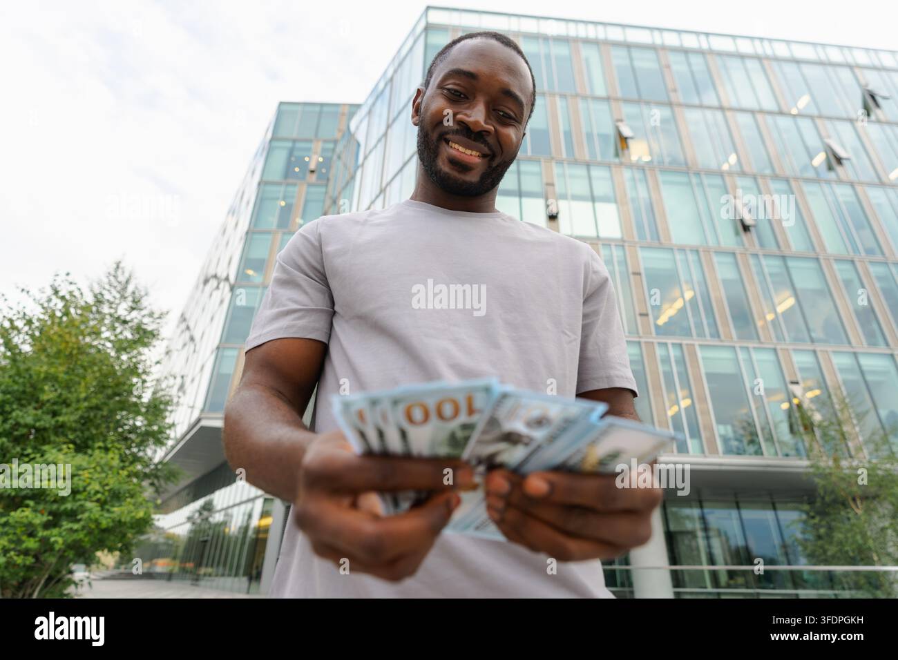 Homme afro-américain tenant des billets d'argent en dollars dans la rue urbaine en ville. Homme d'affaires comptant l'argent de papier monnaie à l'extérieur près de l'immeuble de la banque de bureau. Homme tenant de l'argent. Finance Economy Banking Banque D'Images