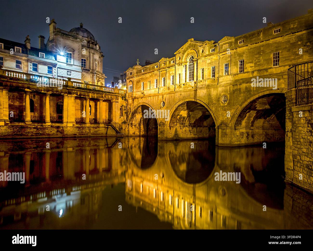 Vue nocturne tranquille et sereine de la ville de Bath au Royaume-Uni avec une architecture dorée et des réflexions colorées scintillant dans la rivière Banque D'Images
