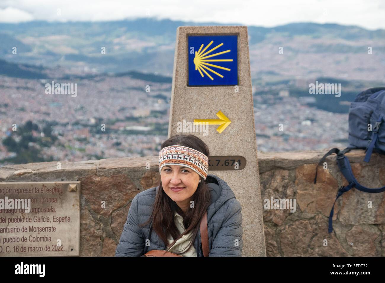 Une pèlerine souriante est assise près d'un marqueur en coquille de Saint-Jacques et d'une flèche jaune du Camino de Santiago au sanctuaire de Monserrate, surplombant Bogotá, Colombie Banque D'Images