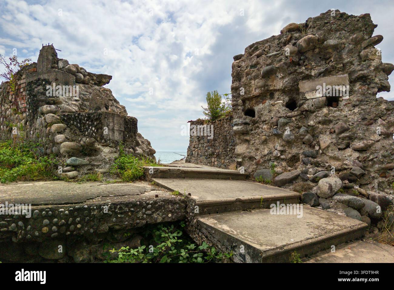 Une prise de vue en extérieur en journée de ruines côtières abandonnées présentant des murs épais construits en béton et en grosses pierres arrondies. Des marches en béton dans le p Banque D'Images