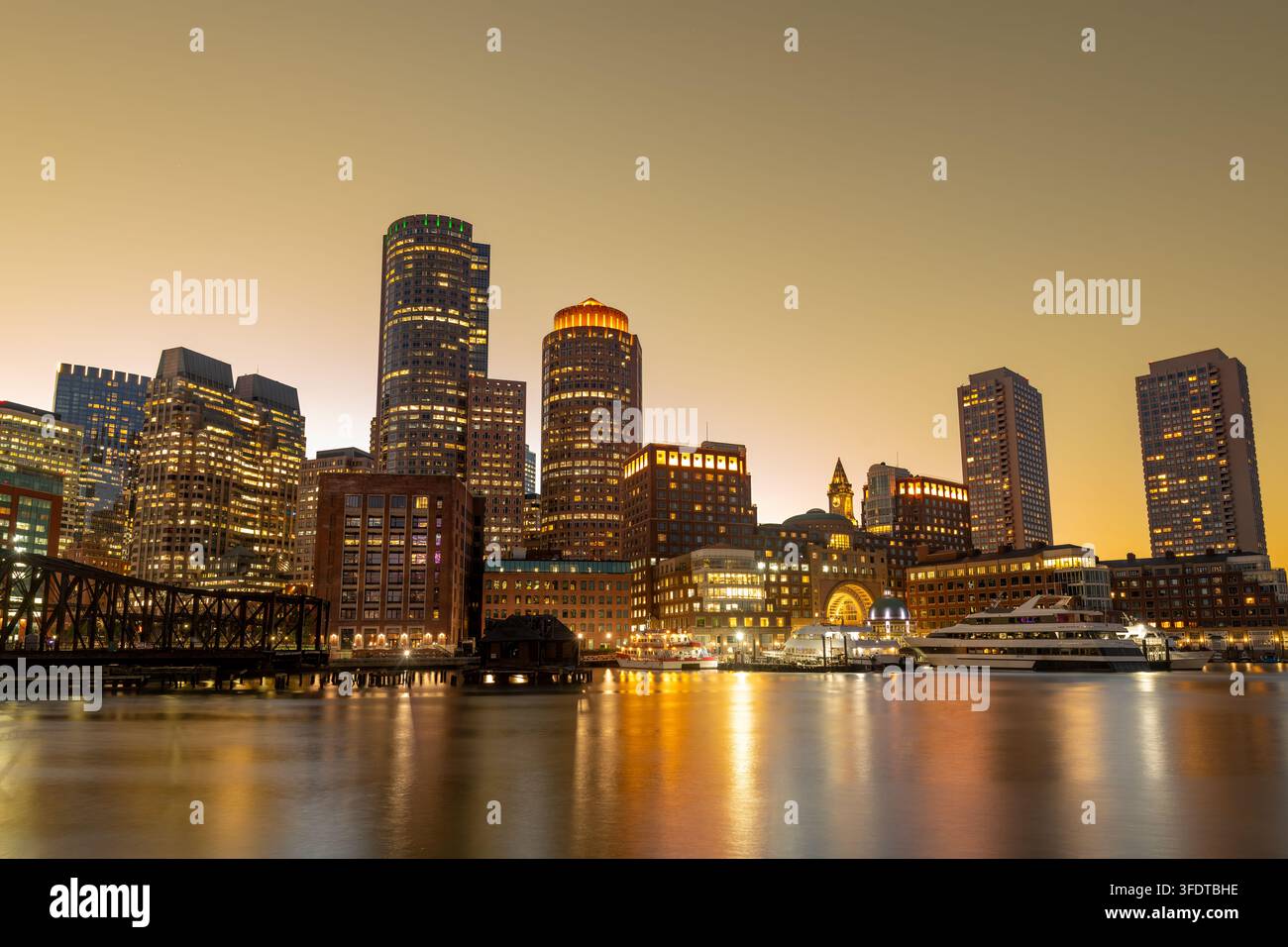 La skyline du centre-ville de Boston au coucher du soleil vue depuis le dynamique Seaport District, mettant en valeur les bâtiments lumineux du quartier financier le long de l'eau du port Banque D'Images