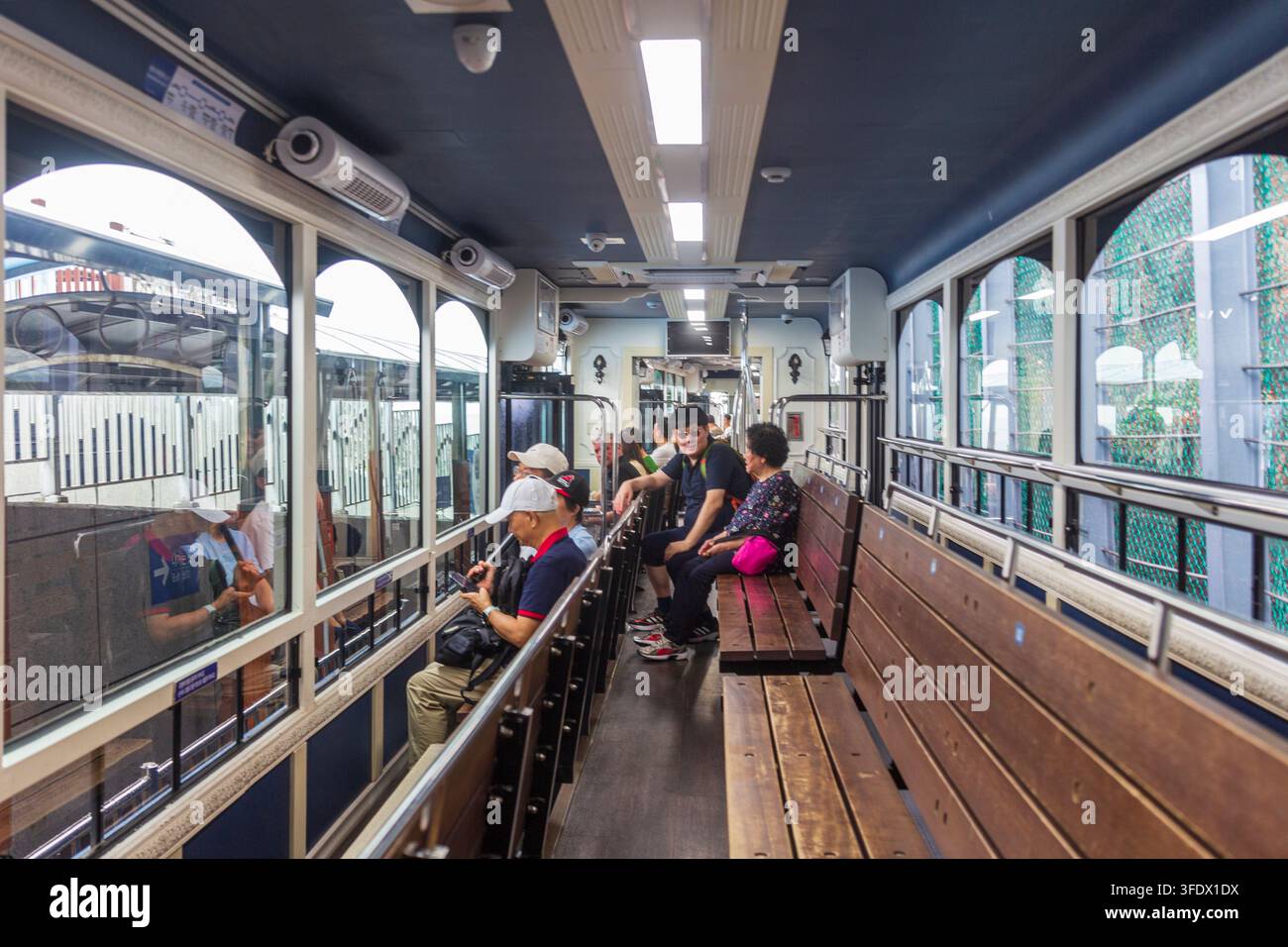 Les passagers voyagent à l'intérieur d'un véhicule de transport public doté de ventilateurs au plafond, de grandes fenêtres, de sièges et de réflexions superposées dans la vitre. Banque D'Images