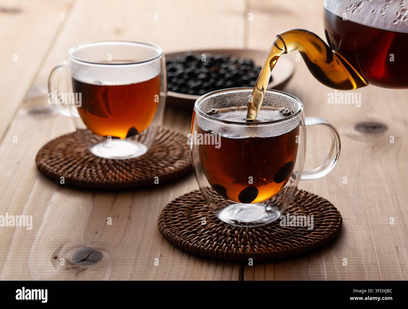 Versement de thé noir chaud au soja d'une théière en verre dans une tasse en verre à double paroi Banque D'Images