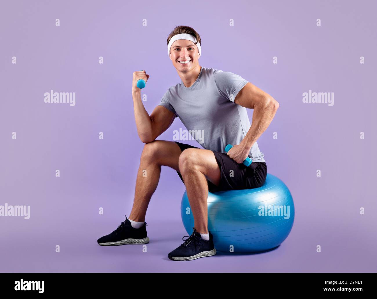 Jeune homme en vêtements de sport assis sur un ballon de fitness et soulevant des haltères Banque D'Images