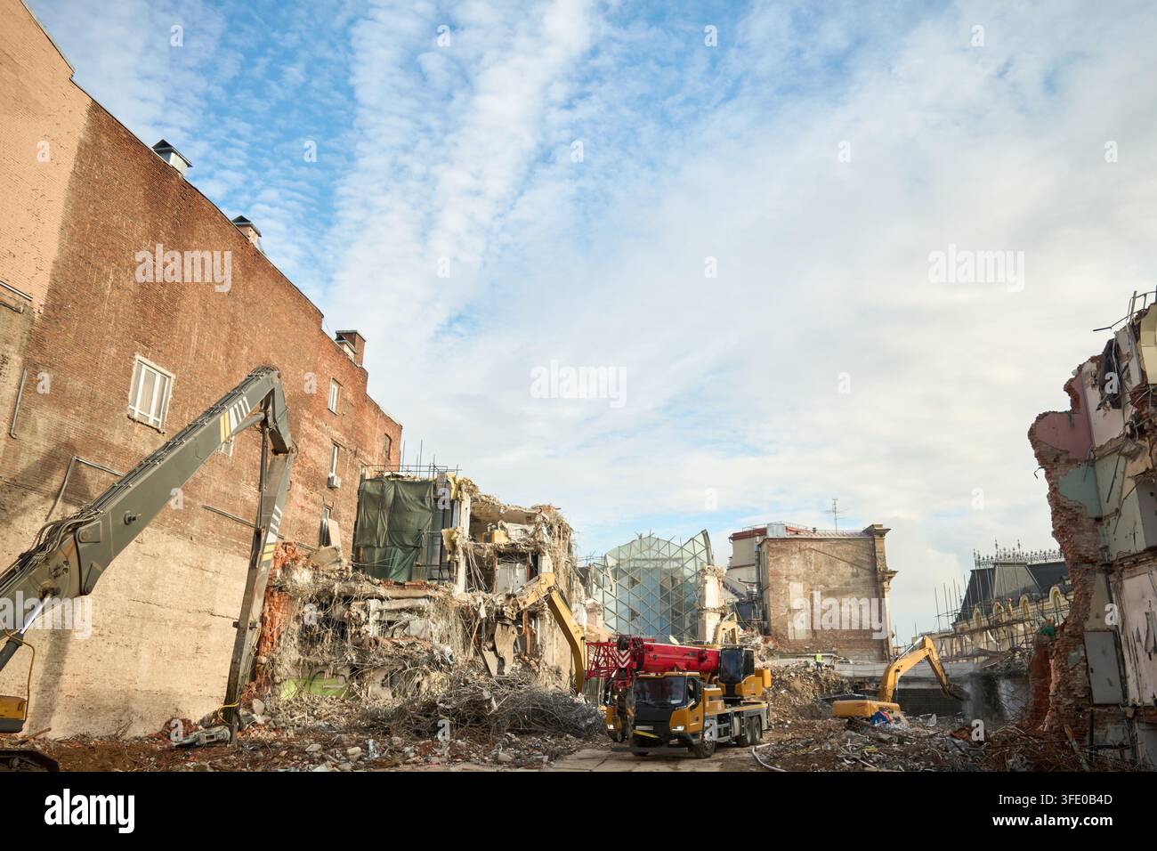 Site de démolition urbain avec des engins de chantier sous un ciel bleu montrant un bâtiment en brique exposé et des gravats, avec démolition, gravats, pelleteuse, détail de grue Banque D'Images