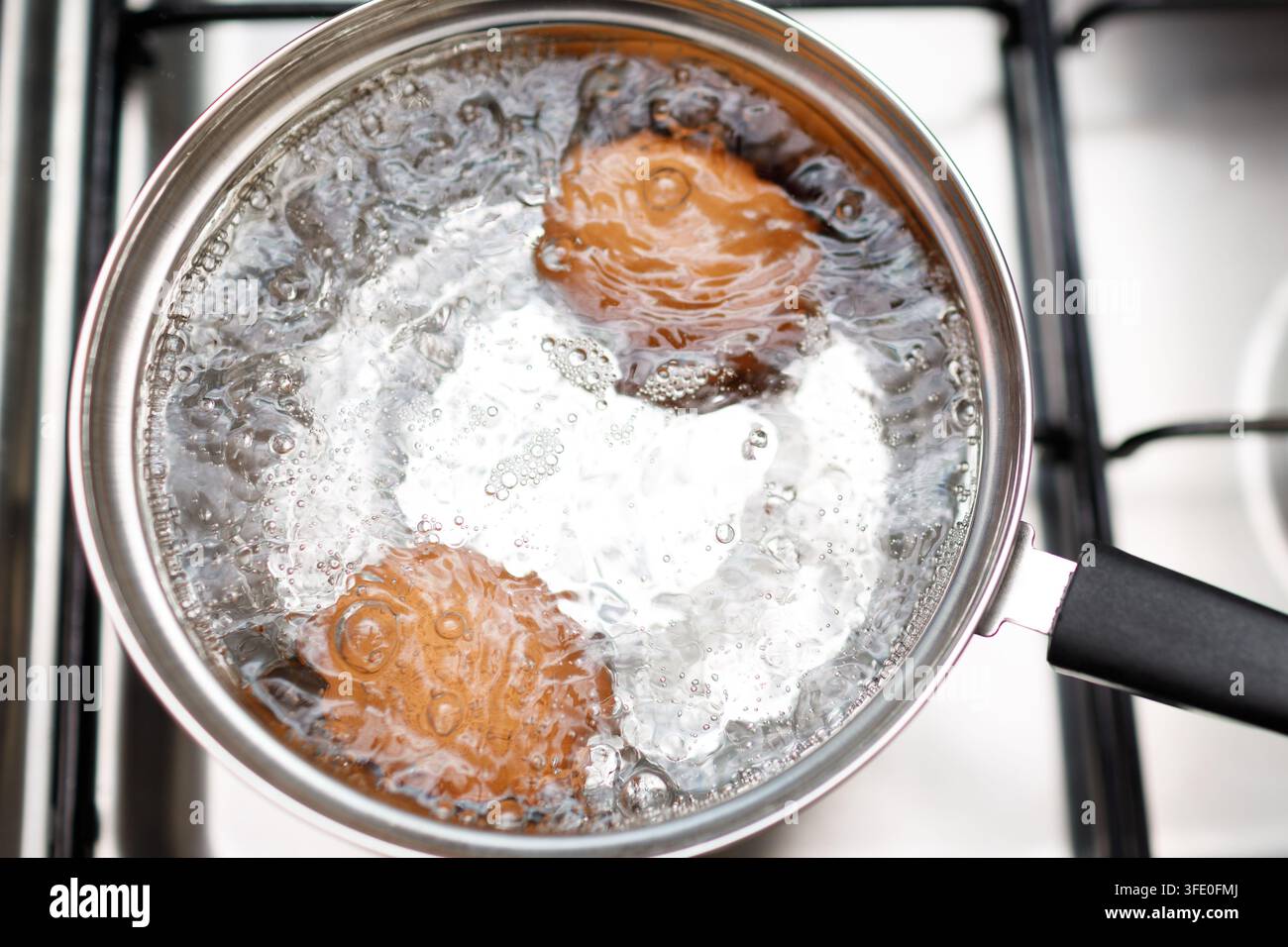 Casserole en acier inoxydable avec des œufs bouillants petit déjeuner dans une eau sur une cuisinière à gaz Banque D'Images