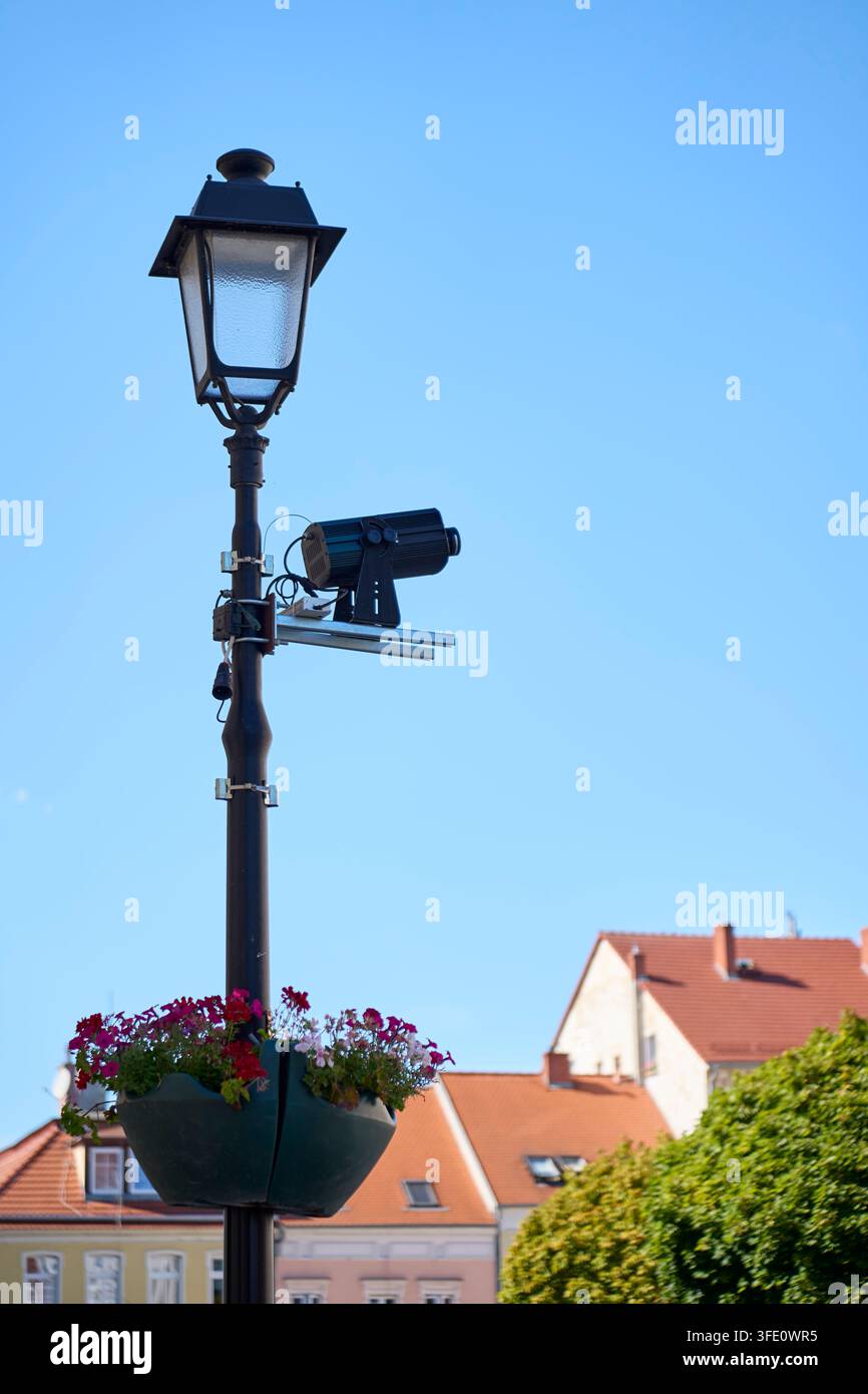 Projecteur vidéo monté sur un lampadaire au-dessus d'un bac à fleurs sur la place de la ville. Concept de projection extérieure, événement public et infrastructure urbaine Banque D'Images