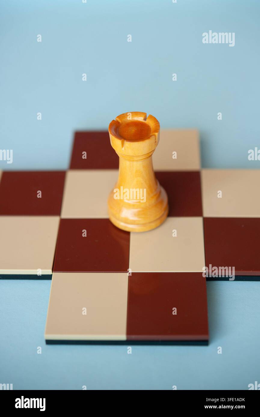 Close-up d'un pion en bois clair posé sur une petite croix d'échiquier rouge et crème contre un fond bleu pâle Banque D'Images
