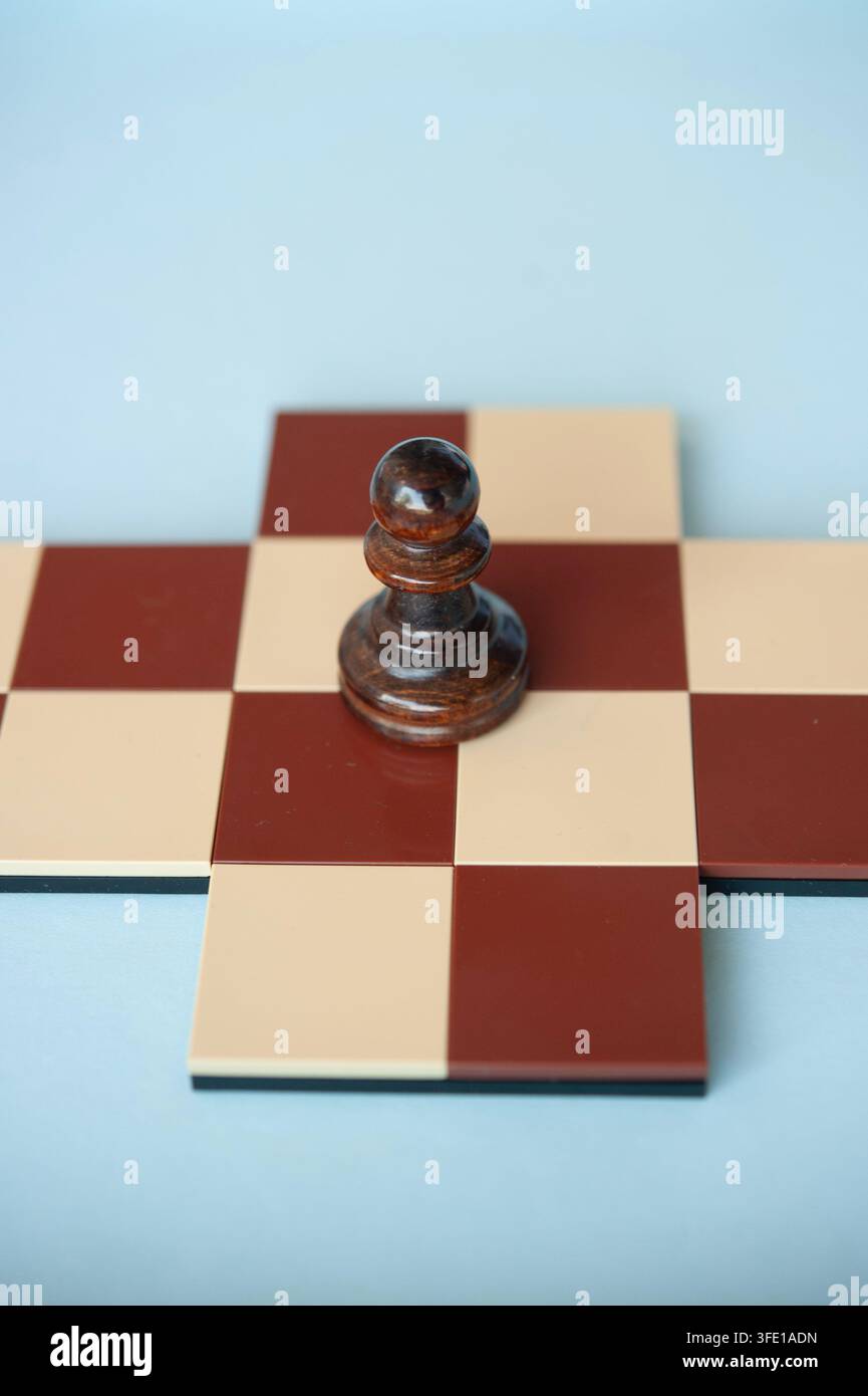 gros plan d'un pion en bois sombre sur une petite croix d'échecs rouge et crème, posé sur un fond bleu pâle Banque D'Images