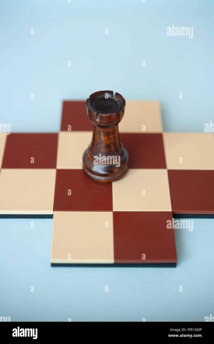 Grossissement d'un pion en bois sombre posé sur une petite croix d'échecs rouge et crème sur un fond bleu pâle Banque D'Images