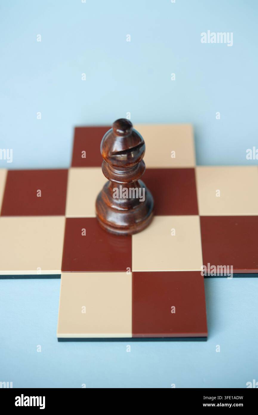 Grossissement d'un évêque en bois sombre posé sur une petite croix d'échecs rouge et crème contre un fond bleu pâle Banque D'Images