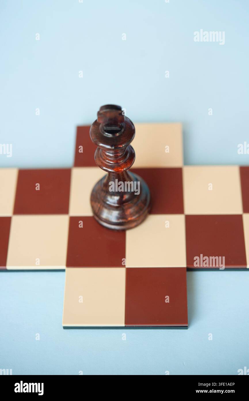 Close-up d'un roi d'échecs en bois sombre debout sur une petite croix d'échecs rouge et crème devant un fond bleu pâle Banque D'Images