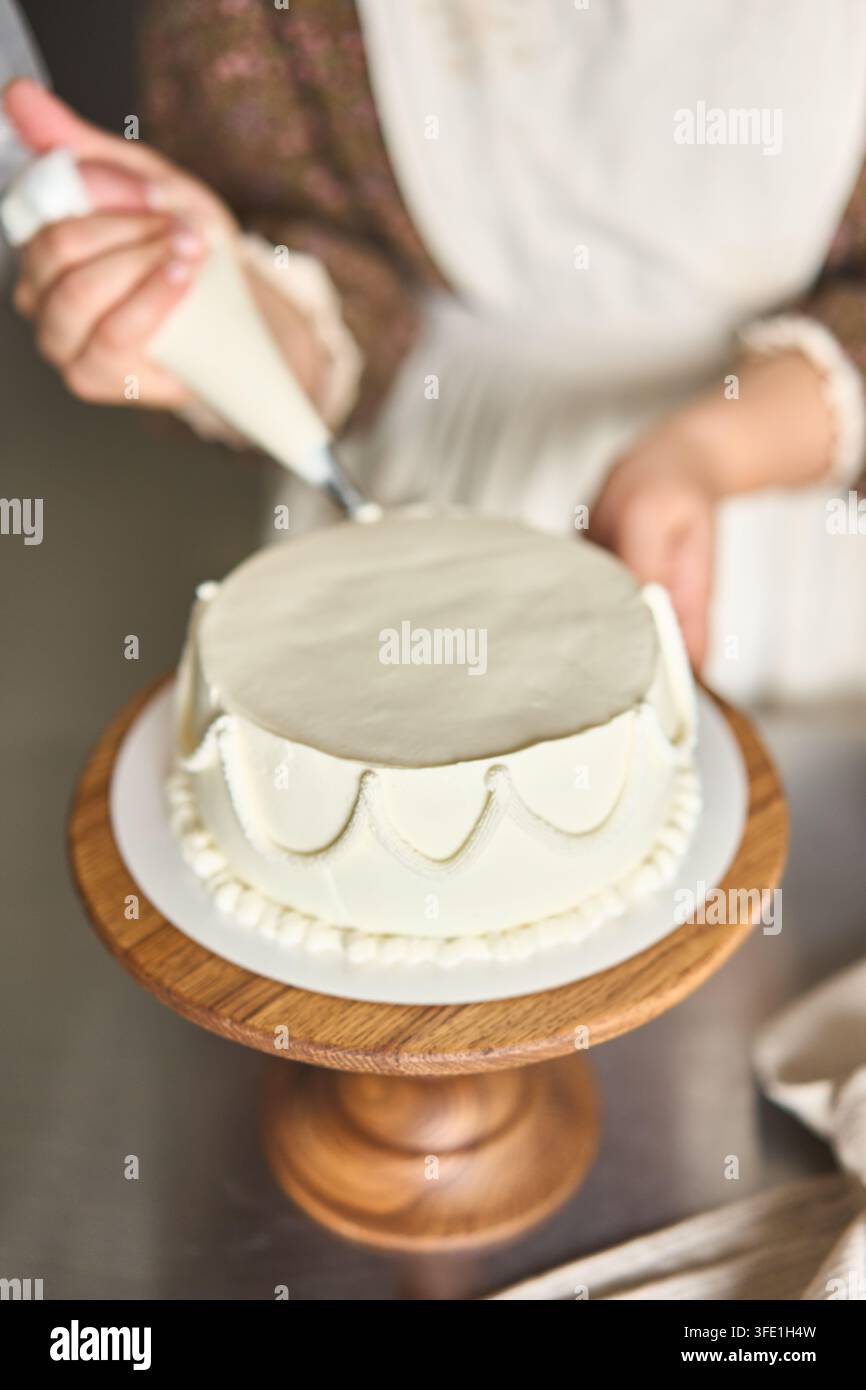 Boulanger dresse une crème fouettée blanche lisse en forme de bordure festonnée sur un gâteau rond de célébration, avec détails de gâteau, glaçage, crème fouettée, glaçage Banque D'Images