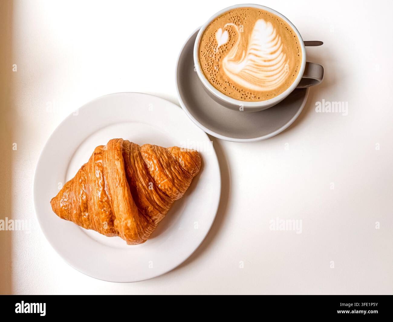Croissant beurré servi avec une tasse de café présentant un art latte en forme de cygne sur une table blanche, photographié de dessus avec espace pour le texte. - Image de stock capturée avec un smartphone