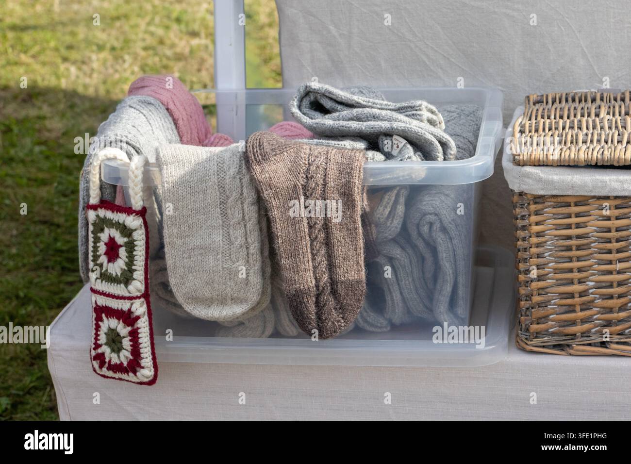 Sélection de chaussettes en laine artisanales soigneusement rangées dans un contenant en plastique transparent et exposées sur une nappe blanche à un marché artisanal en plein air. Traditi Banque D'Images