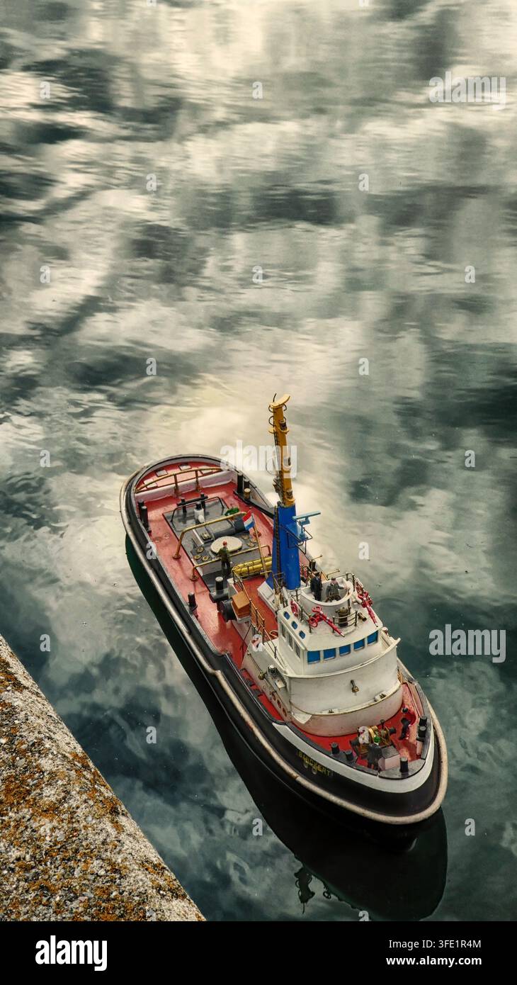 Un bateau de remorquage radiocommandé avec un ciel dramatique se reflétant dans l'eau Banque D'Images