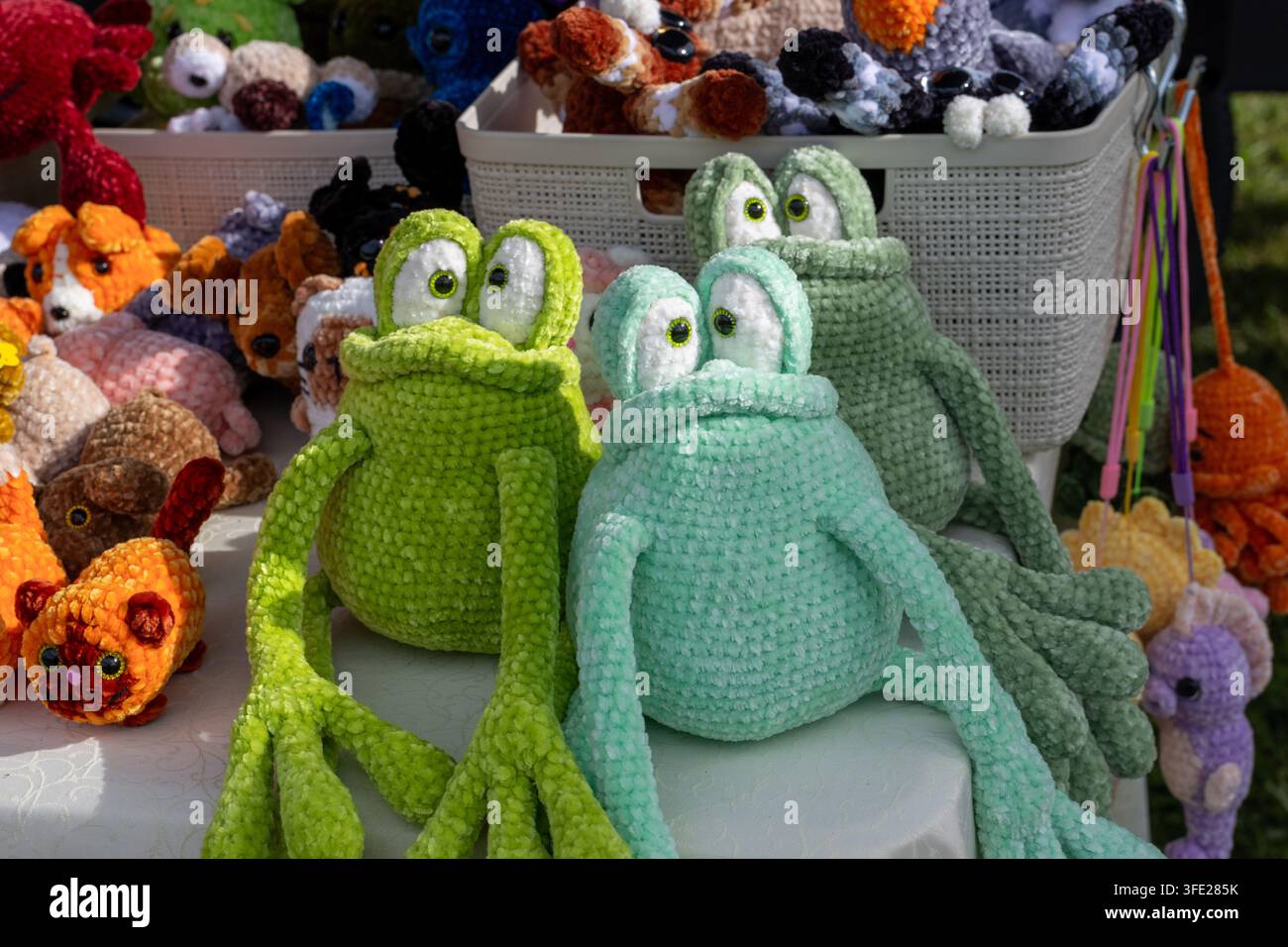 Vue rapprochée de grenouilles en peluche amigurumi tricotées à la main, exposées sur une table d'un marché artisanal en plein air. La collection d'artisanat présente du chenille doux Banque D'Images
