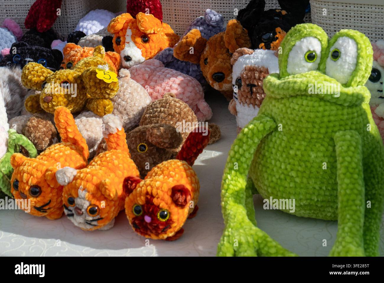 Vue rapprochée d'une grande grenouille en peluche verte crochetée assise à côté d'une variété d'animaux amigurumi fabriqués à la main sur une table d'exposition en plein air Banque D'Images