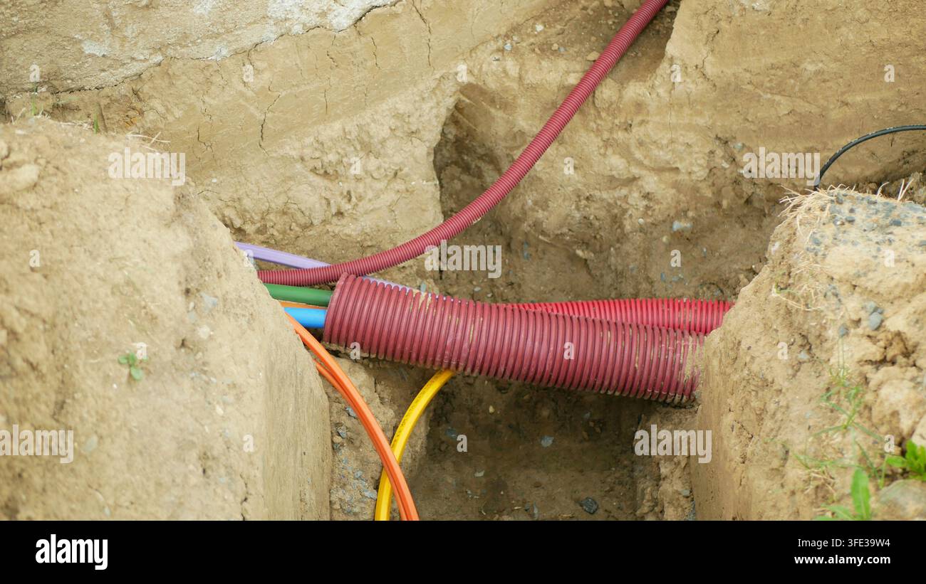 Câbles d'infrastructure Internet en fibre optique cuivre ingénierie réseaux conduits pose installée sous terre excavé sol tranchée construction Banque D'Images