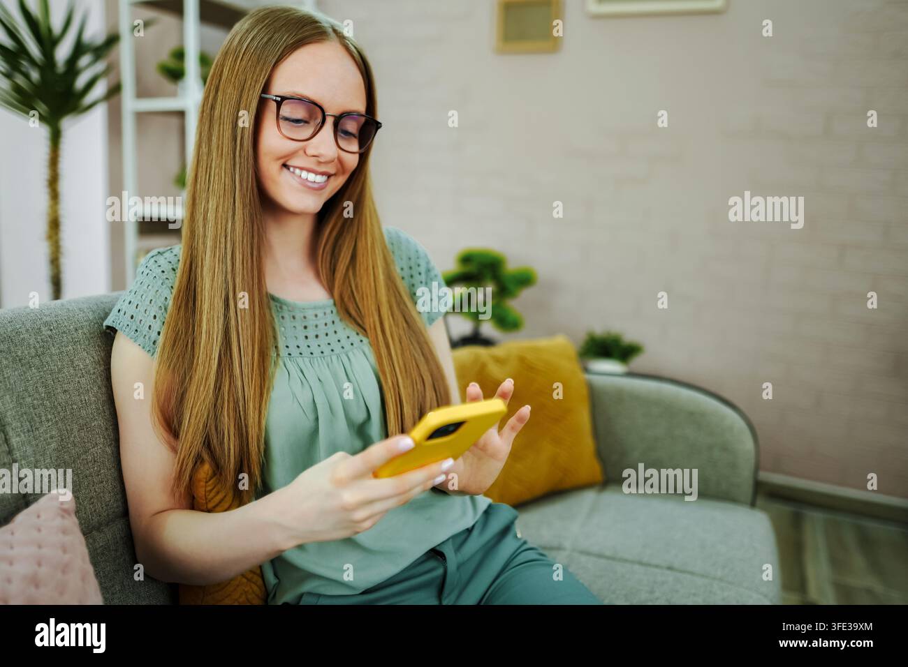 Jeune femme souriante utilisant un smartphone assise sur un canapé Banque D'Images