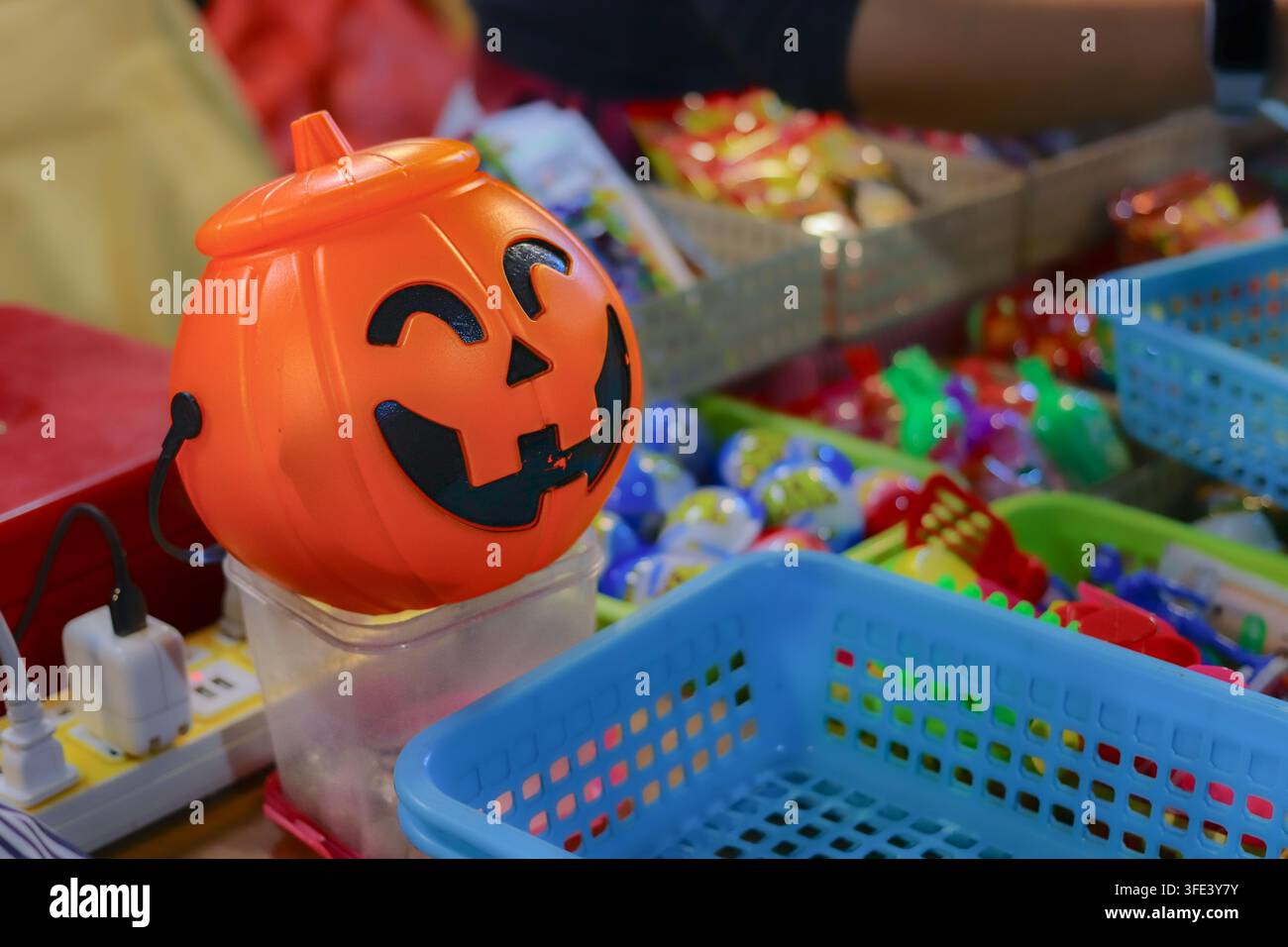 Seau en plastique orange en forme de lanterne à côté de paniers de jouets colorés et de paquets de bonbons sur un étal de marché de nuit. Banque D'Images