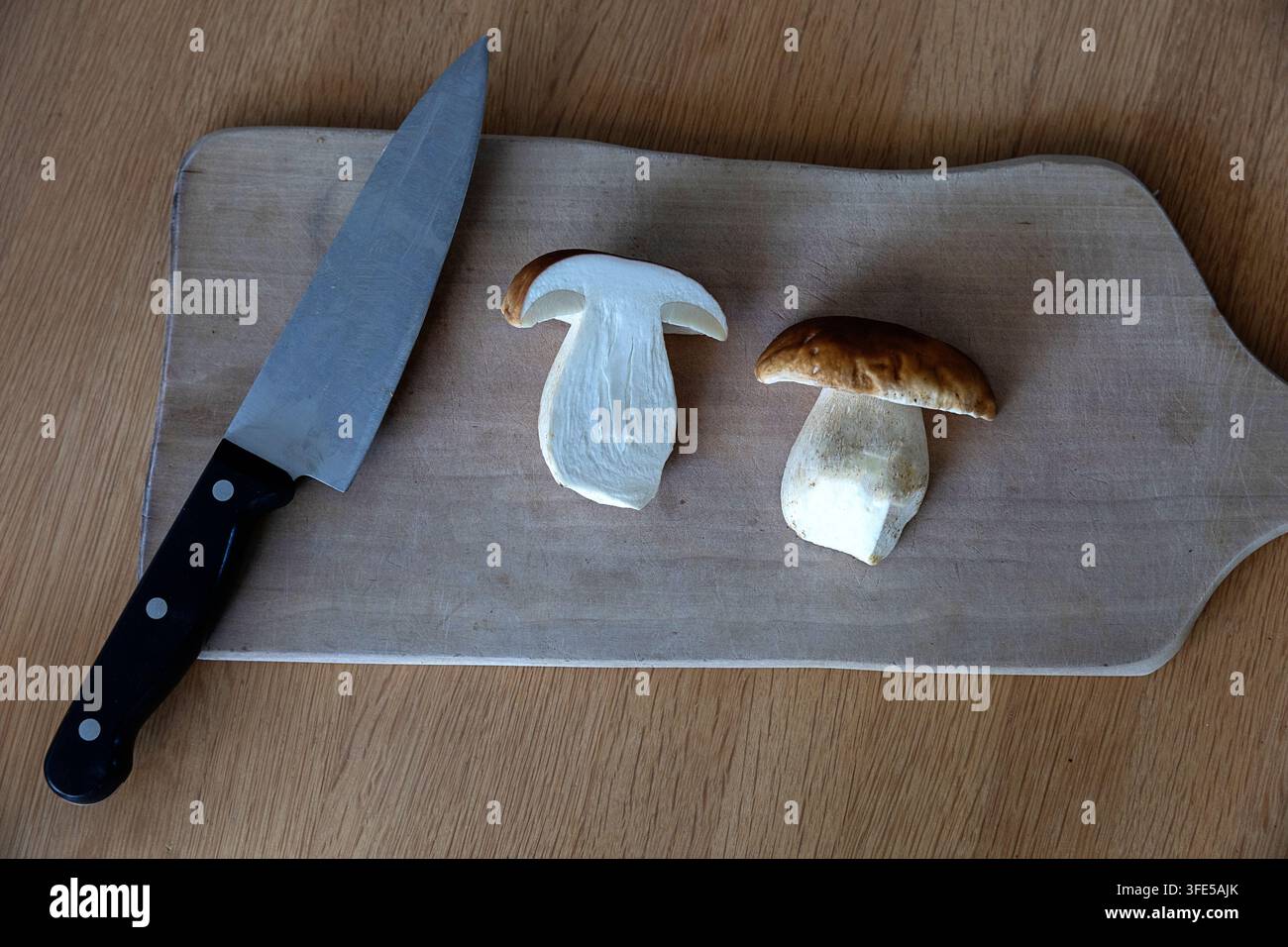 Un plan rapproché détaillé d'un champignon porcini frais coupé en deux sur une planche à découper rustique en bois, avec un couteau de cuisine professionnel à côté. Banque D'Images
