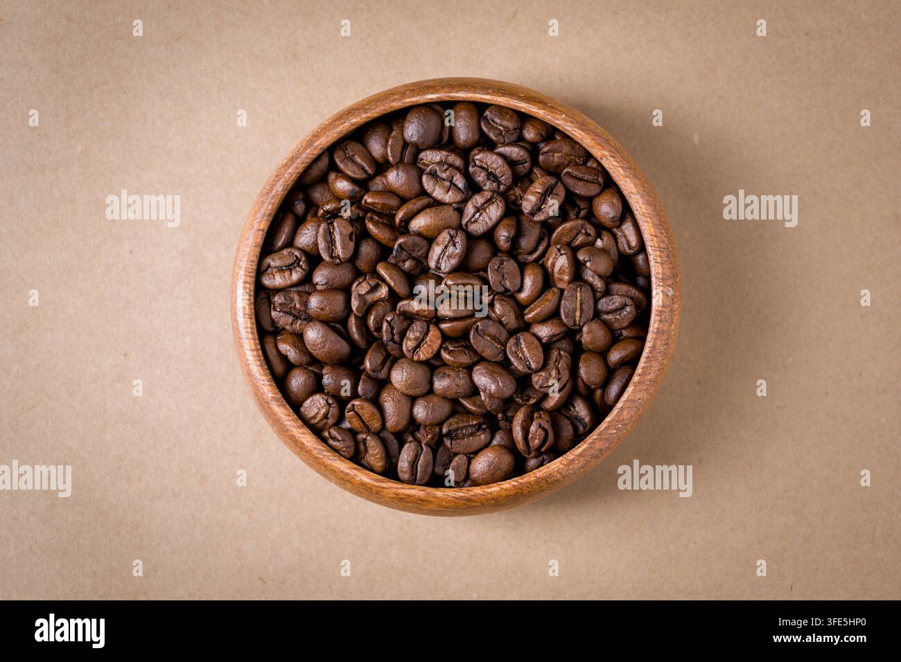 Vue supérieure de grains de café torréfiés dans un bol en bois sur un fond kraft Banque D'Images