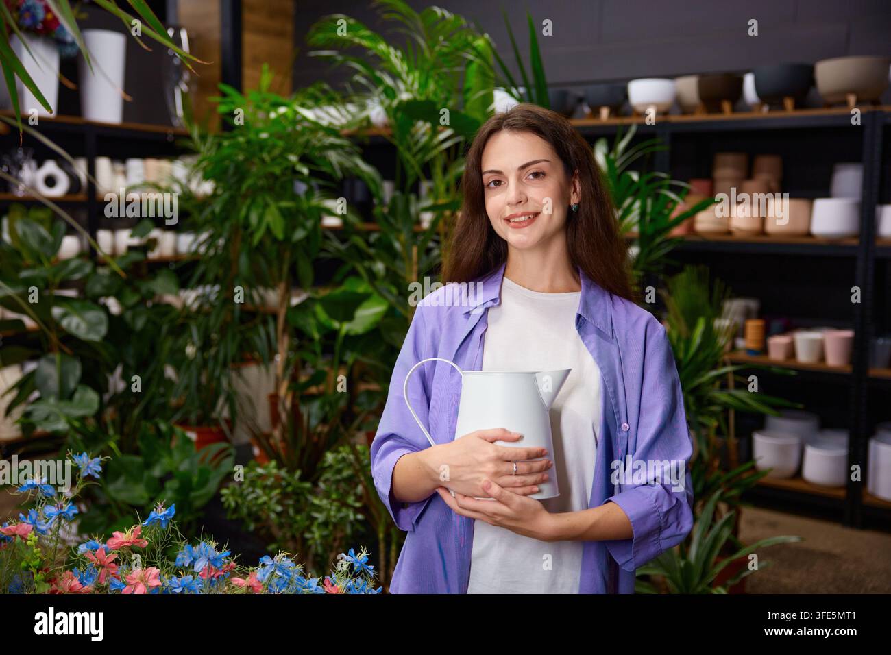 Femme tenant un vase en céramique dans un atelier boutique avec des étagères en arrière-plan Banque D'Images