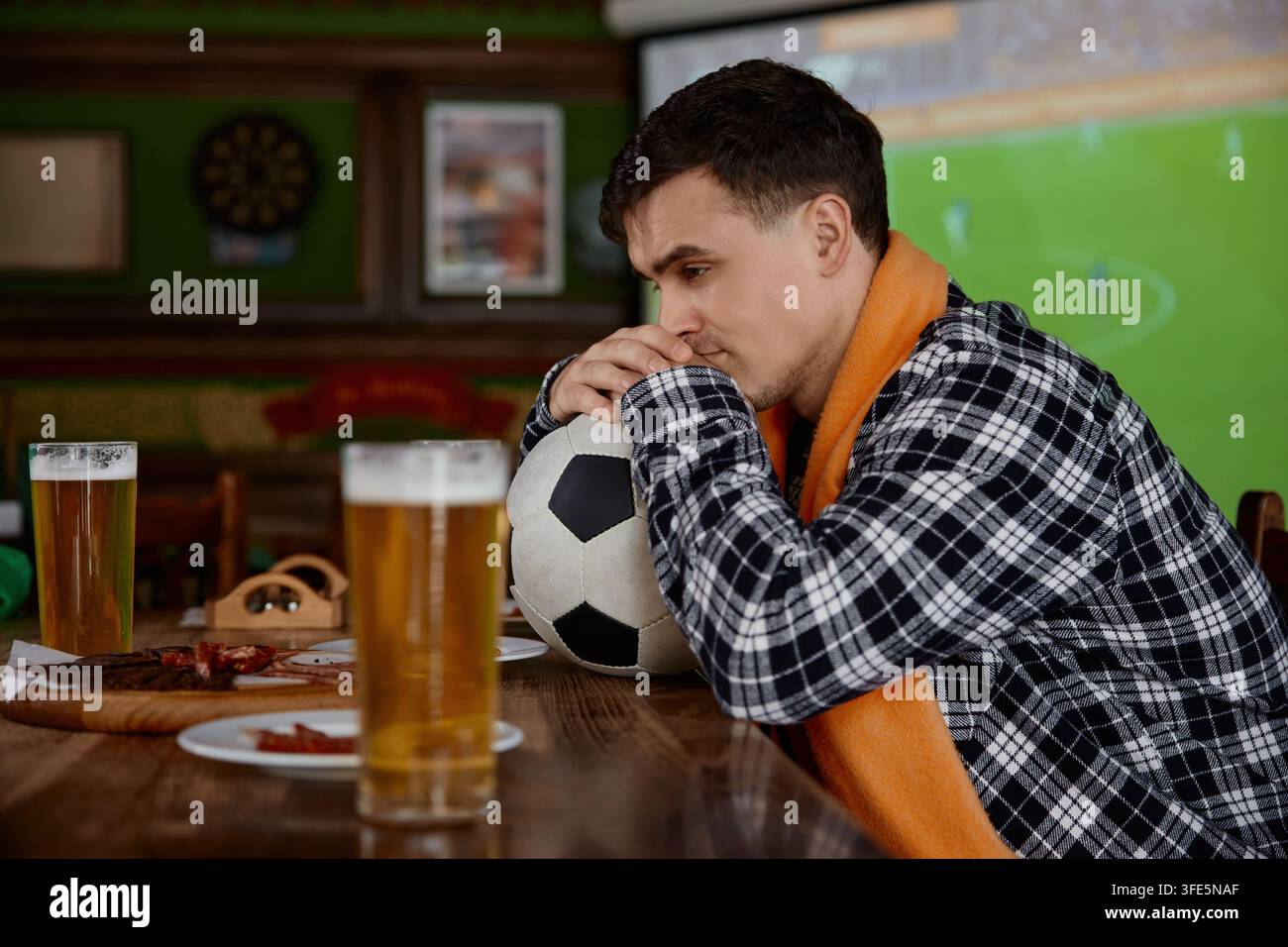Passionné de sport anxieux serrant fermement le ballon avec un regard concentré lors de la diffusion en direct passionnante Banque D'Images