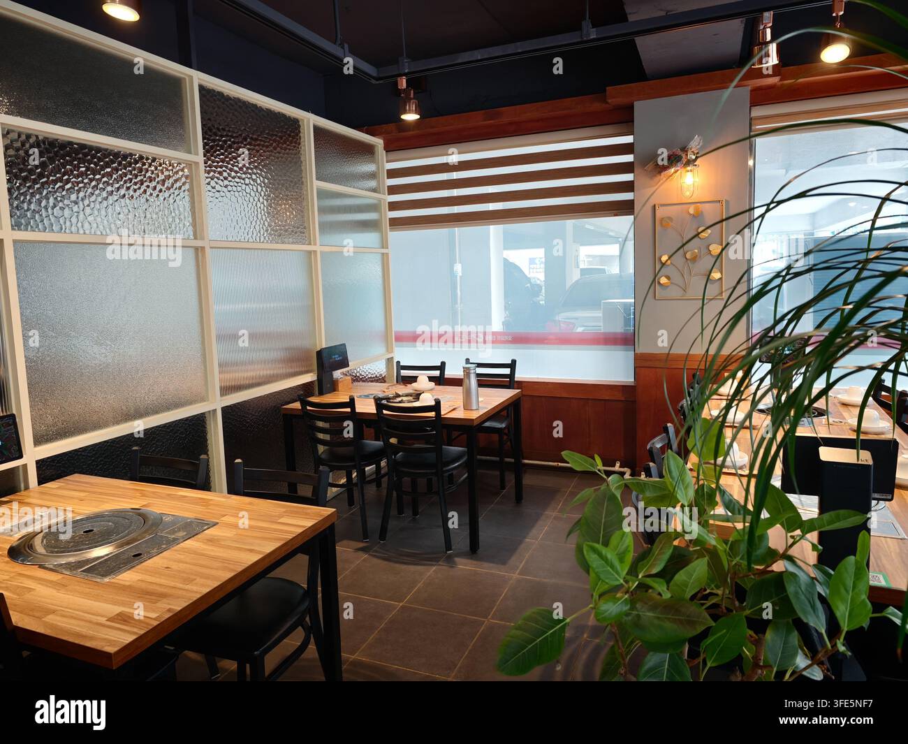 Intérieur moderne d'un restaurant coréen en Corée avec des tables en bois, des chaises noires, des plantes et des cloisons en verre dépoli. Banque D'Images
