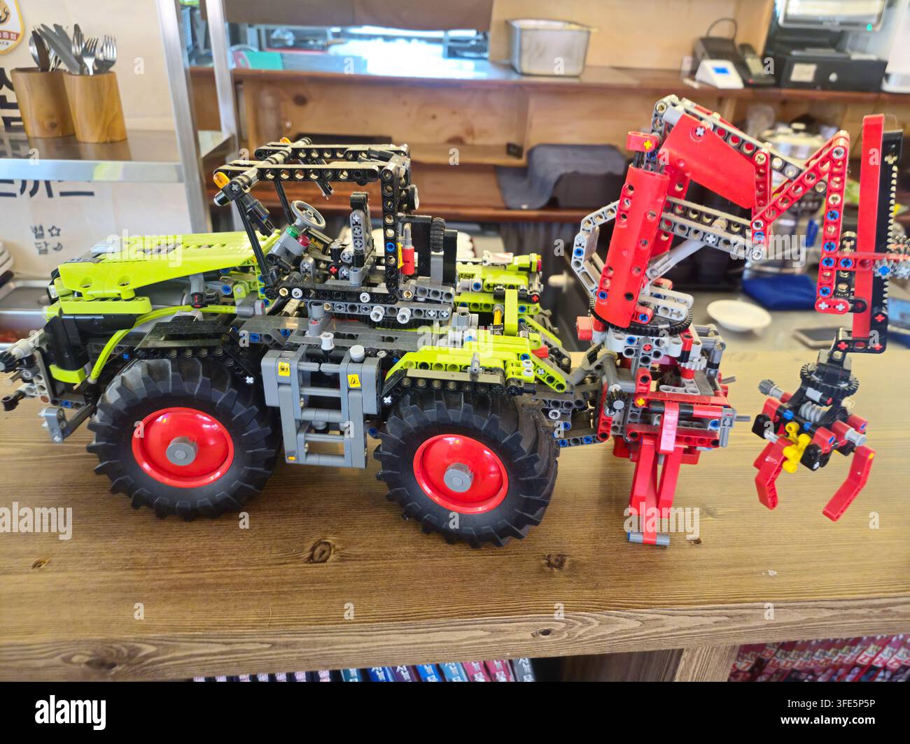 Gros plan d'un modèle de tracteur LEGO Technic coloré avec un bras mécanique rouge sur une surface en bois à l'intérieur. Banque D'Images