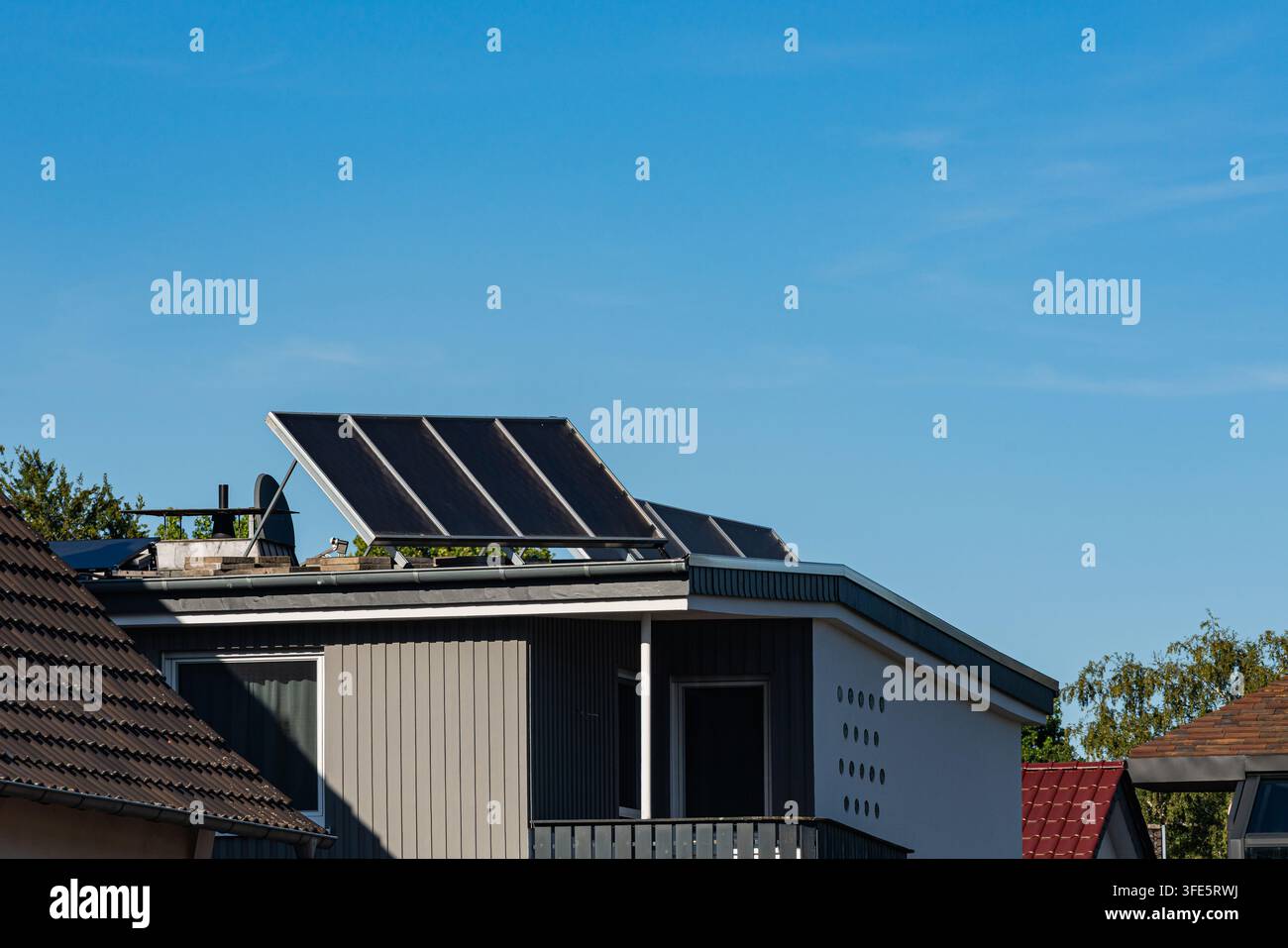 Des panneaux solaires sont placés sur le toit d'une maison. La scène montre un ciel bleu clair avec quelques nuages. La maison est située dans un quartier résidentiel avec arbre Banque D'Images