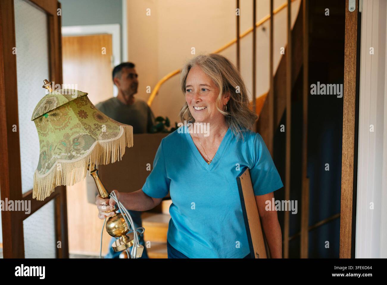 Femme souriante tenant un cadre photo et une lampe tout en emménageant dans son nouveau logement Banque D'Images