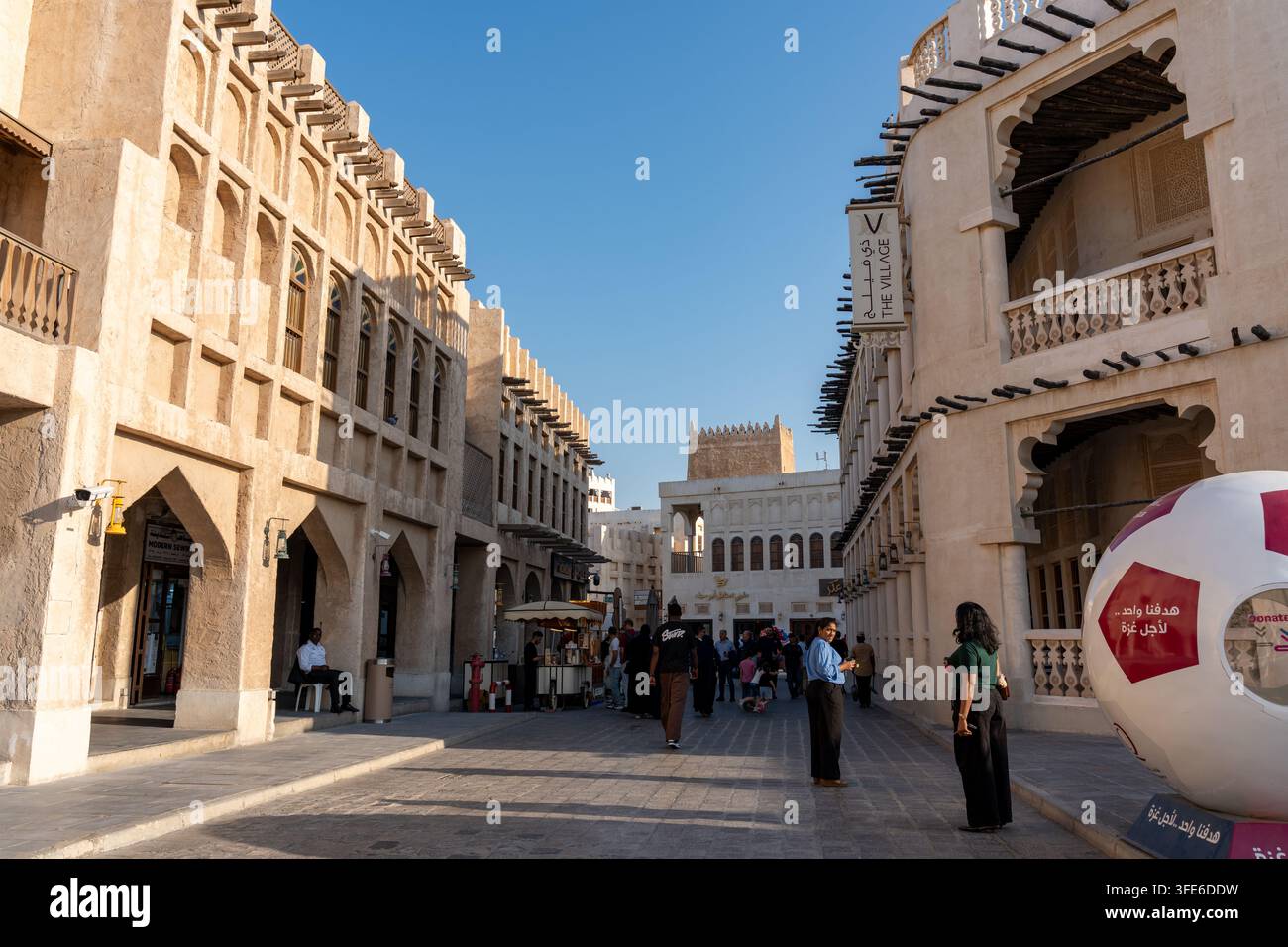 Doha, Qatar - 14 février 2026 : Une vue en perspective à un point large de touristes explorant une rue piétonne pavée devant The Village Restaurant. Banque D'Images