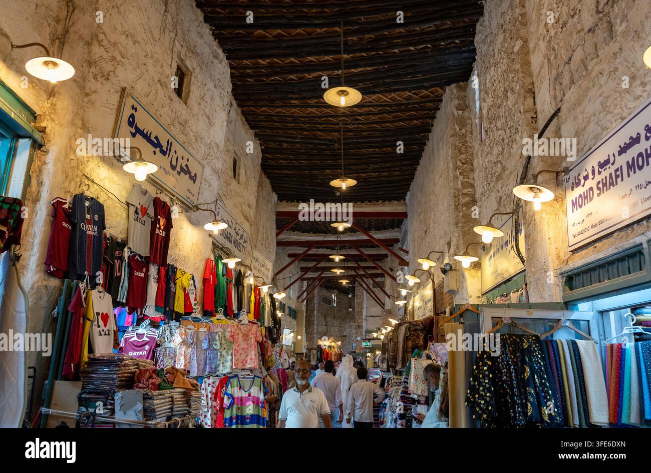 Doha, Qatar - 14 février 2026 : Vue en perspective en un point regardant vers le haut d'une allée de marché textile couverte et animée bordée de stands de vêtements colorés. Banque D'Images