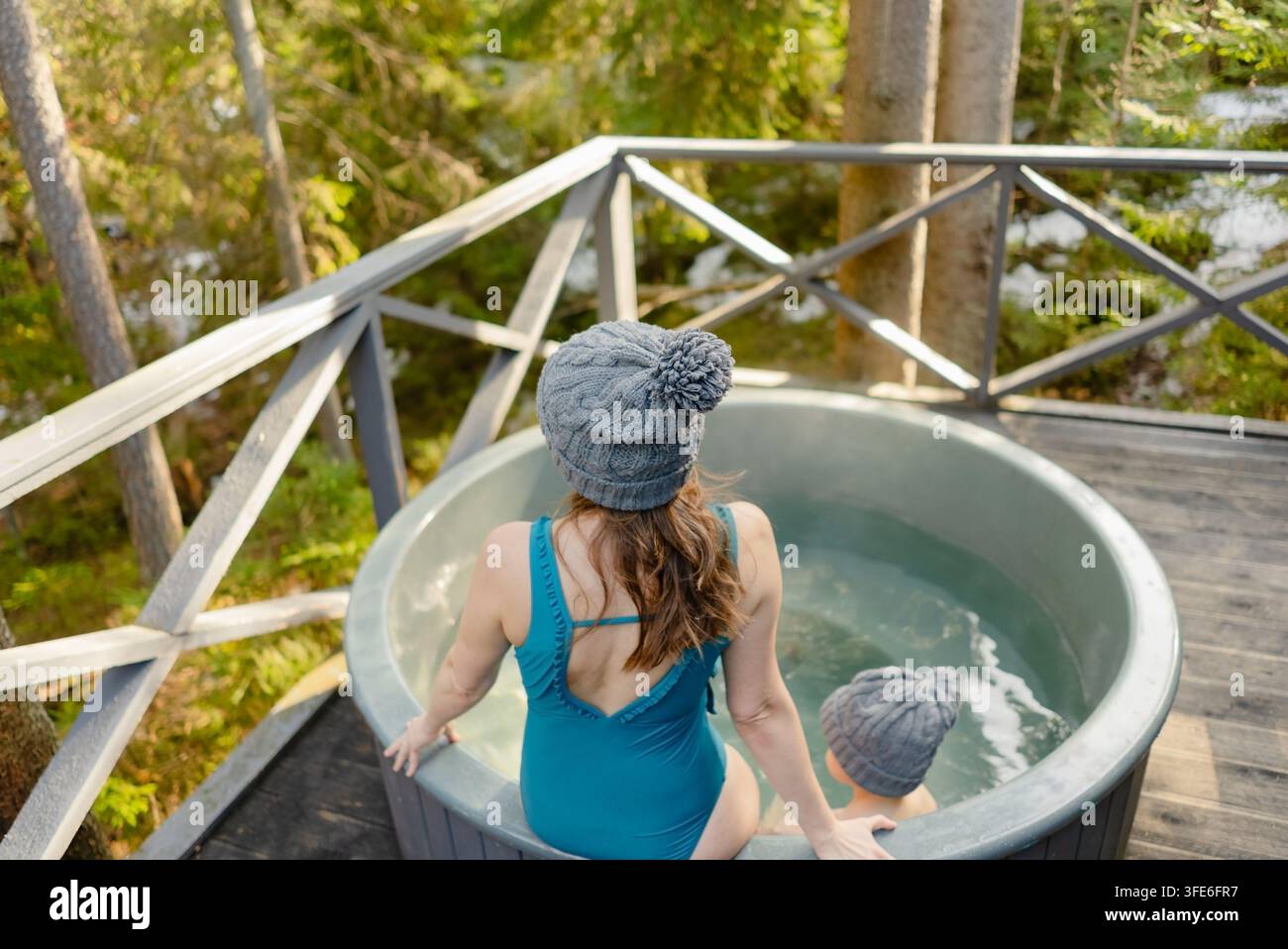 Une femme confiante se tient dans un jacuzzi sur une terrasse en bois, se détendant tout en profitant de la nature sereine. Cette scène paisible capture un moment agréable de traitements spa en plein air pour une femme adulte calme. Banque D'Images