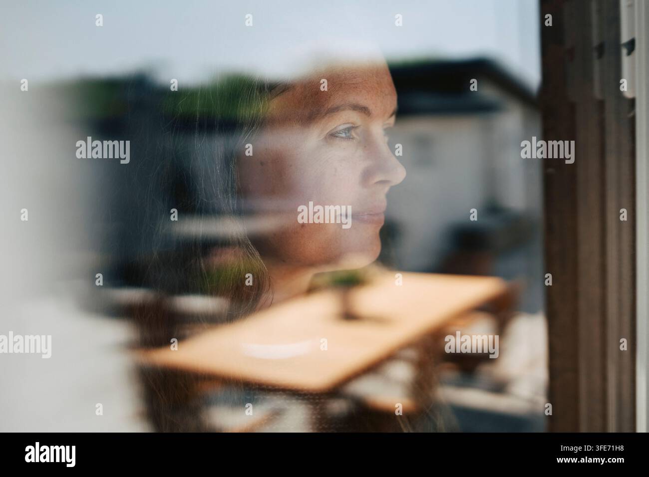 Femme mûre souriante regardant par une fenêtre en verre Banque D'Images