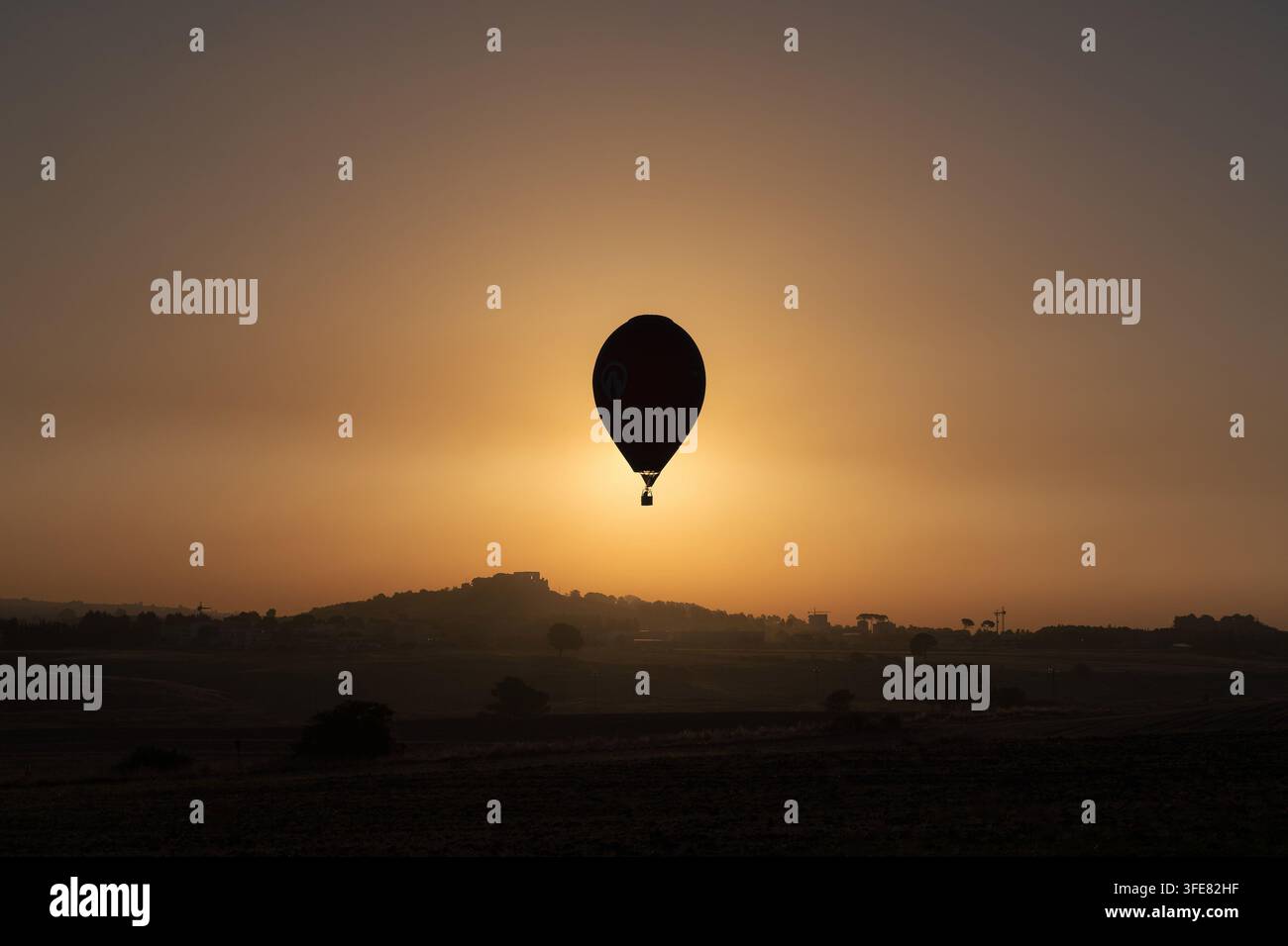 Vue d'un ballon à air chaud en silhouette contre le coucher de soleil doré sur le paysage rural de Gravina in Puglia, Pouilles, Italie. Banque D'Images