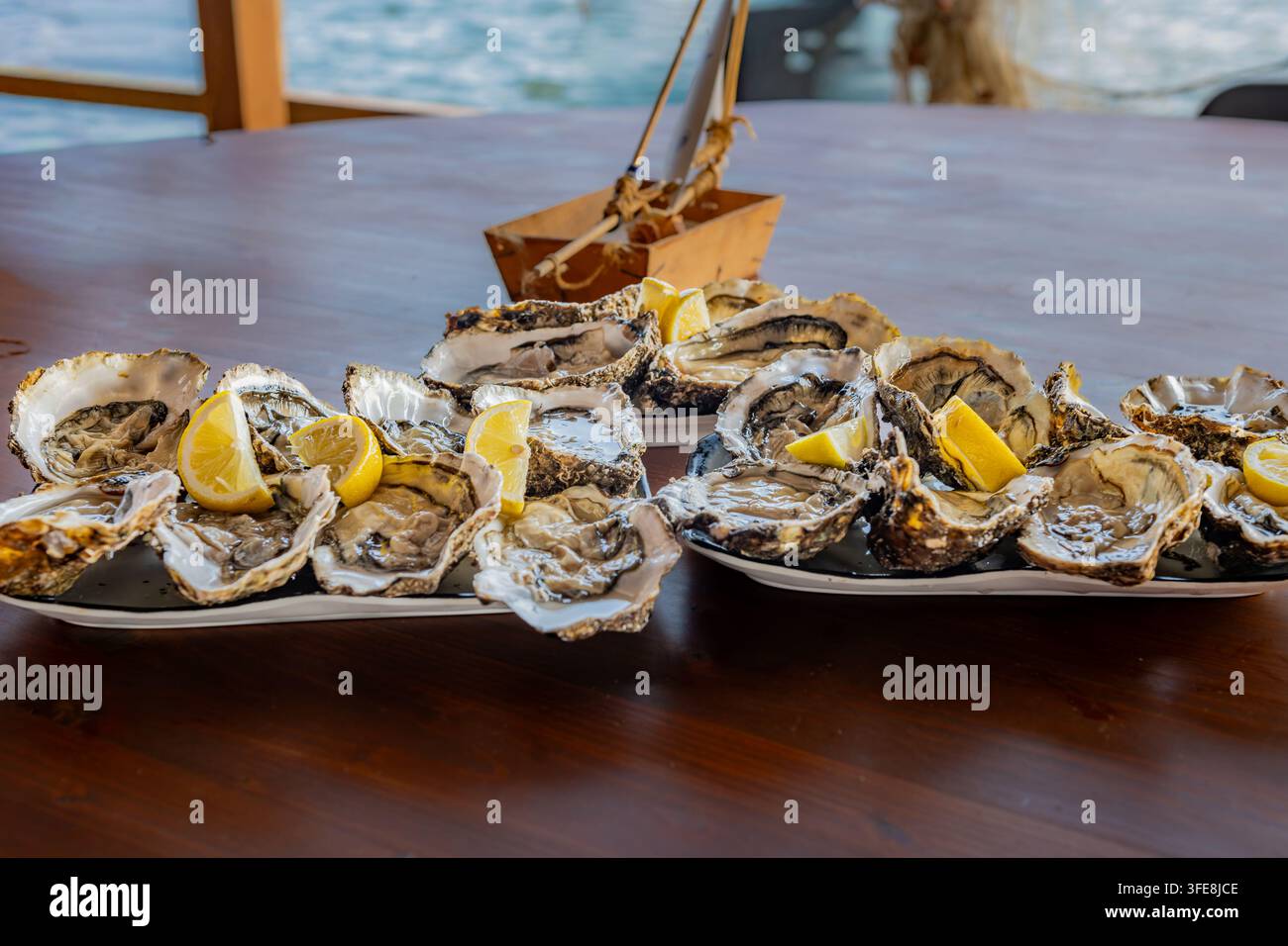 Assiettes d'huîtres fraîchement ouvragées garnies de quartiers de citron sur une table avec un bateau jouet en bois dans le delta de l'Ebre. Banque D'Images
