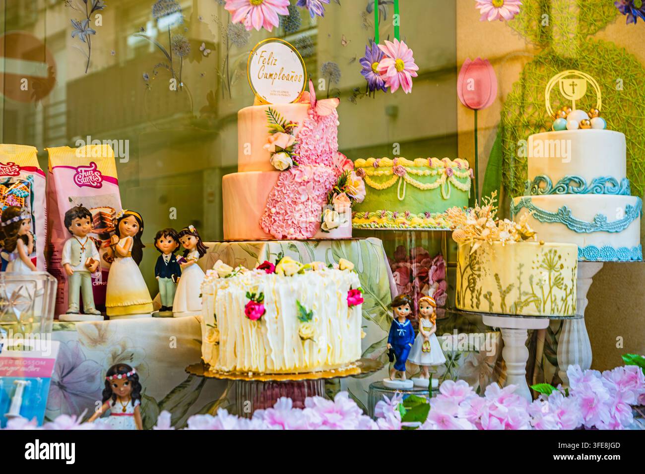 Gâteaux de fête et de communion à plusieurs étages élaborés exposés dans la vitrine d'une boulangerie avec des décorations florales à Reus. Banque D'Images